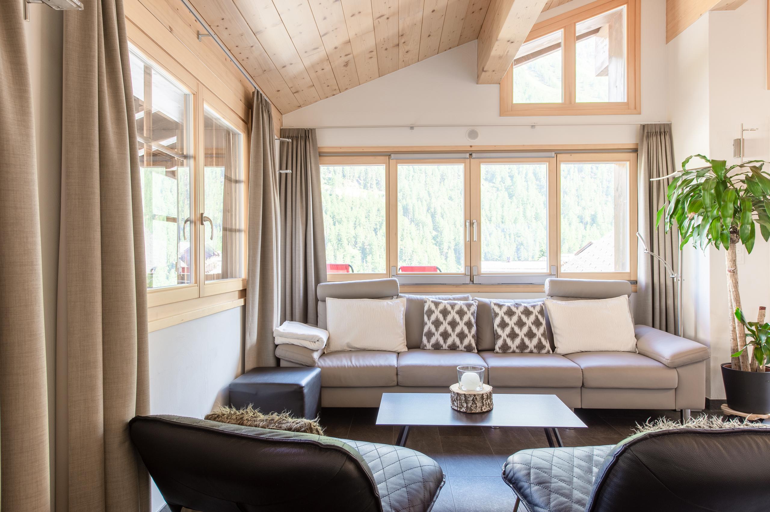 Open lounge area in the Swiss Escape chalet with leather sofas, coffee table, and large windows overlooking the forest