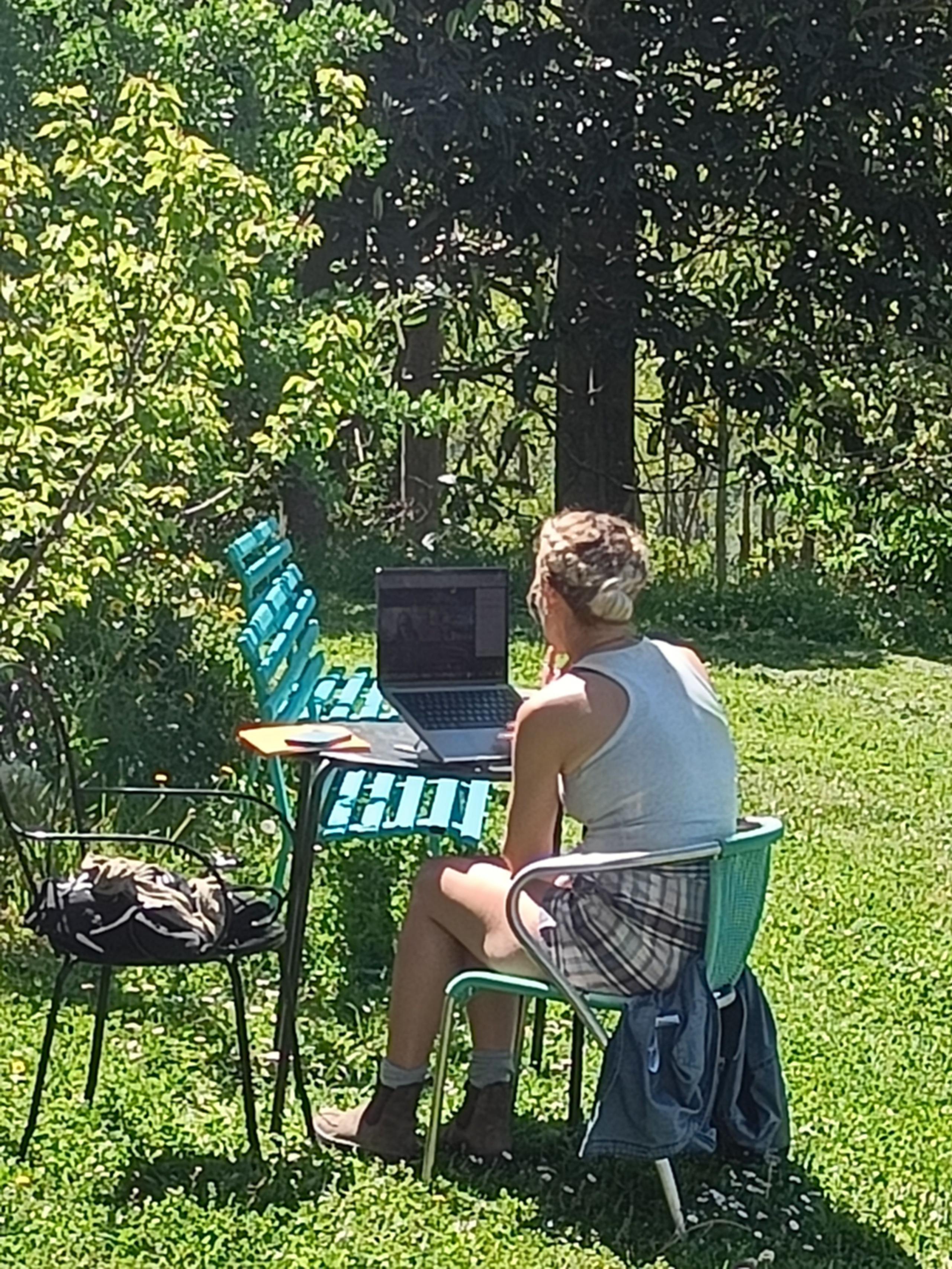 A coliver working on a laptop at a table in the garden, surrounded by lush greenery
