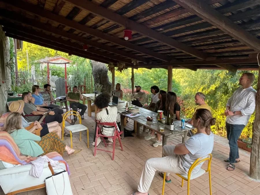 Group meeting or workshop session held under the outdoor pergola, with participants seated around tables