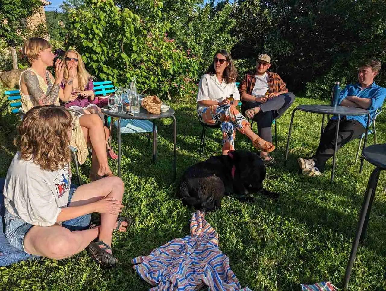 Group of colivers relaxing and socializing in the garden with drinks, with a dog present