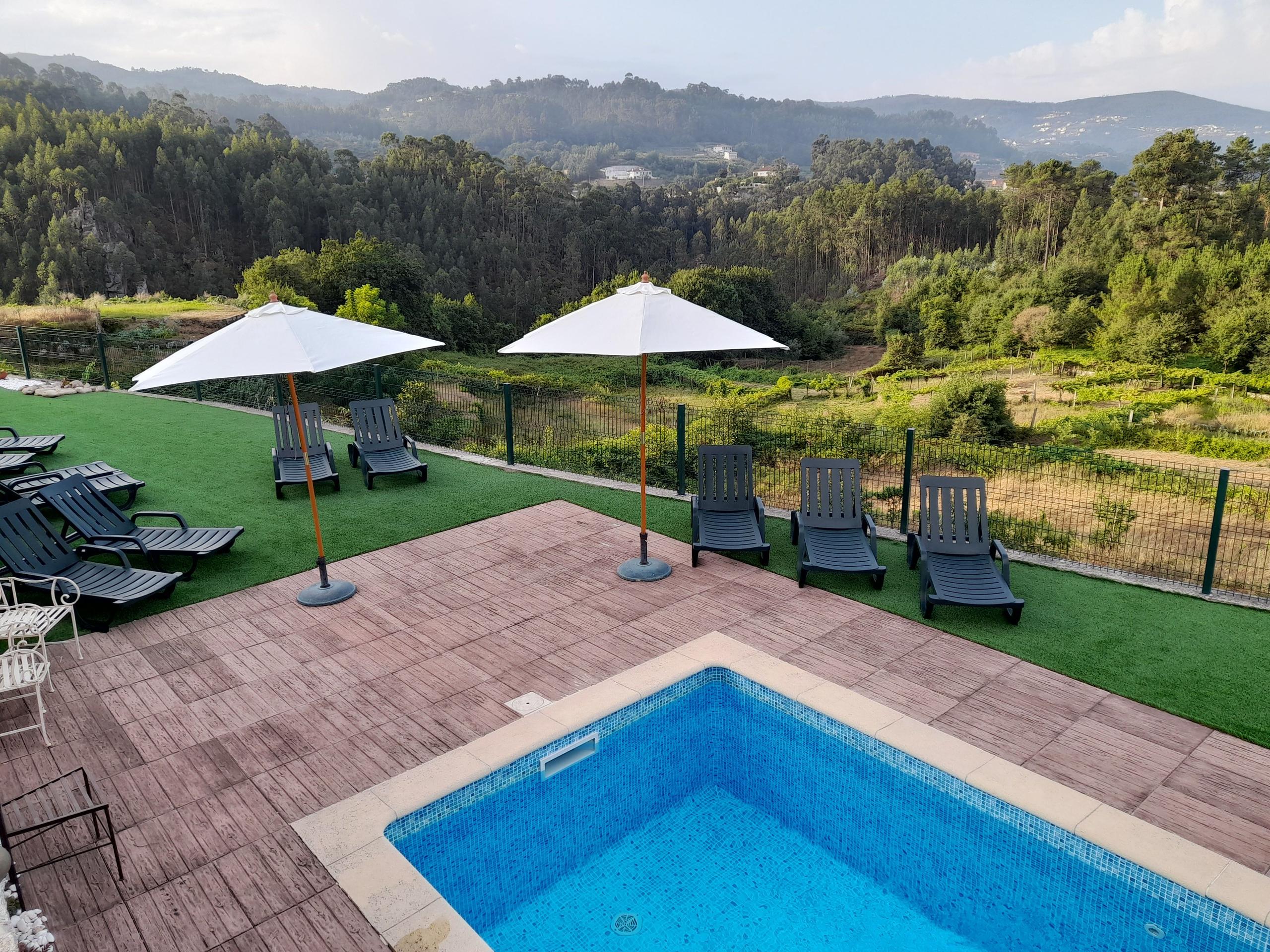 Outdoor swimming pool with sun loungers, parasols and valley/mountain views in the background