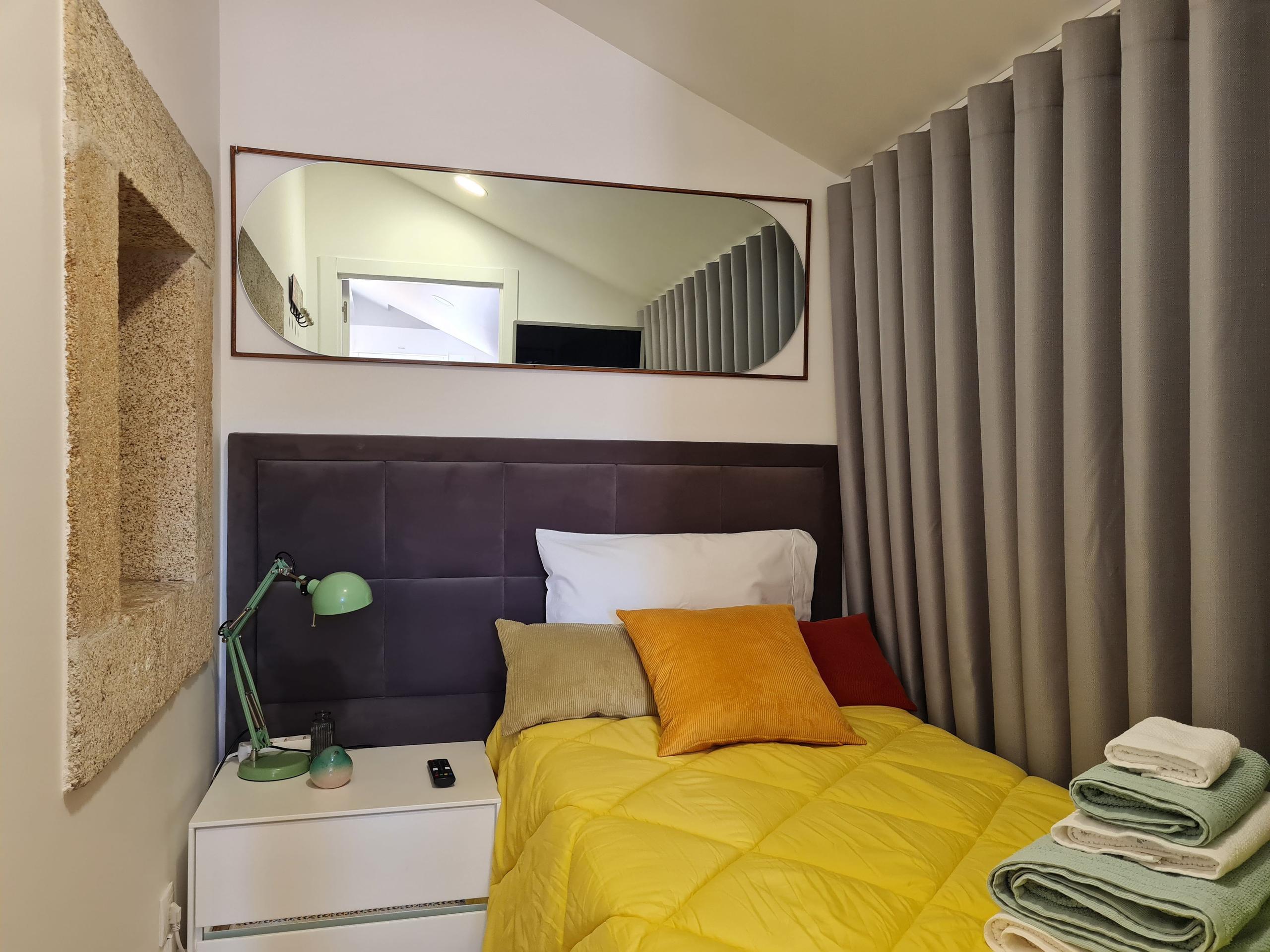 Compact minimalist bedroom with single bed, yellow duvet, mirror and grey curtain divider