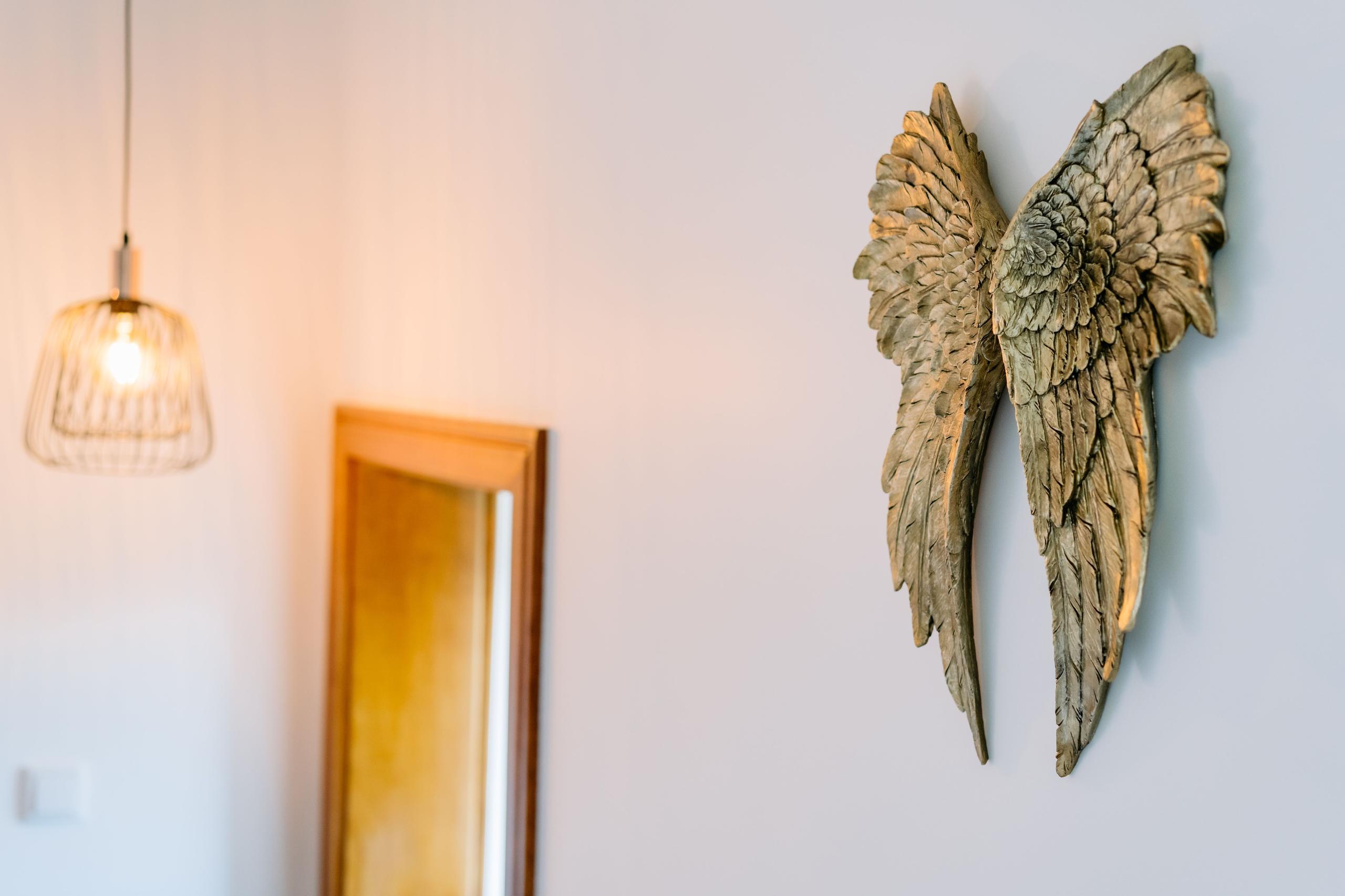 Bedroom interior detail showing decorative angel wings wall art, pendant lamp and full-length mirror