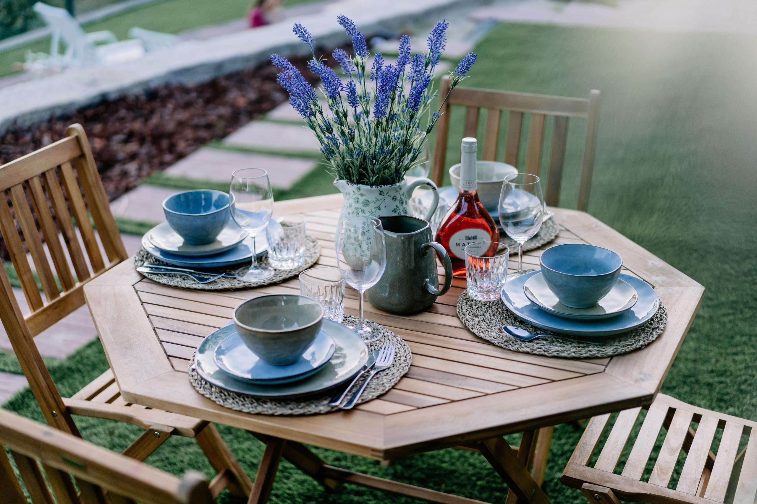 Outdoor wooden octagonal table set with blue tableware, lavender flowers and wine in the garden