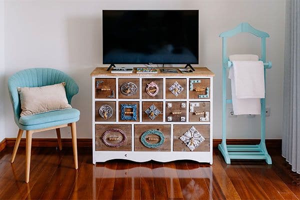 Bedroom interior with decorative wooden dresser, Smart TV, teal armchair and valet stand