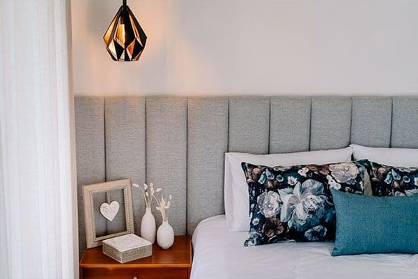 Bedroom with upholstered grey headboard, floral and blue pillows, pendant lamp and bedside table