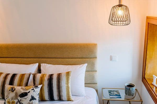 Bedroom with warm-toned upholstered headboard, striped pillows, pendant lamp and bedside table