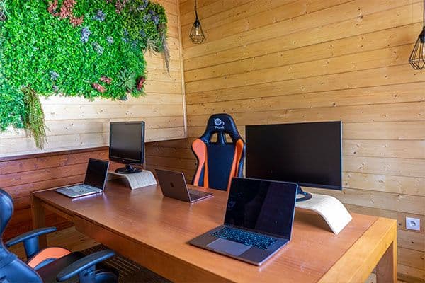 Interior of the coworking wooden cabin with desks, laptops, LCD monitors, ergonomic chairs and a green plant wall