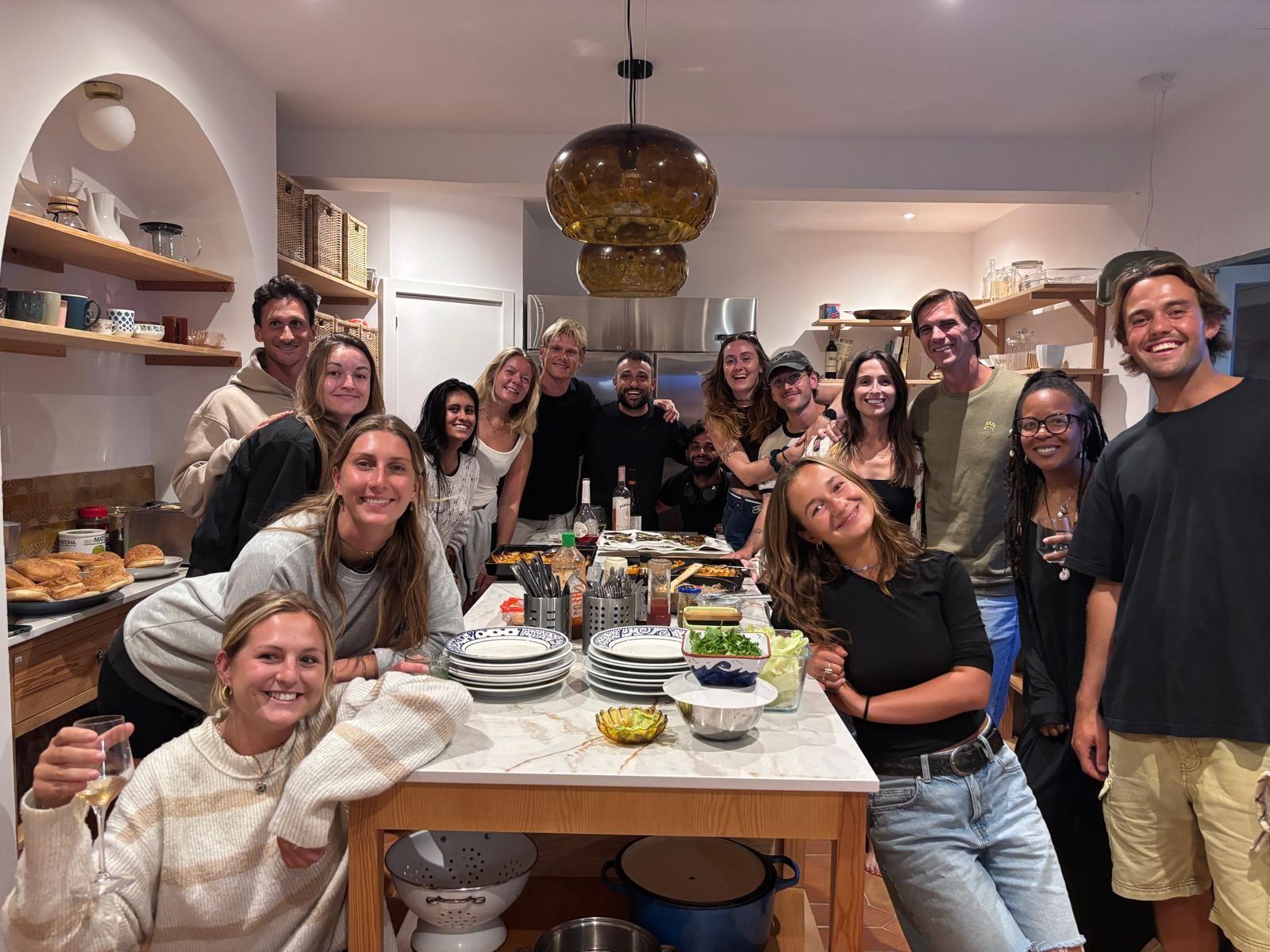 Large group of coliving residents gathered around the kitchen island for a community dinner