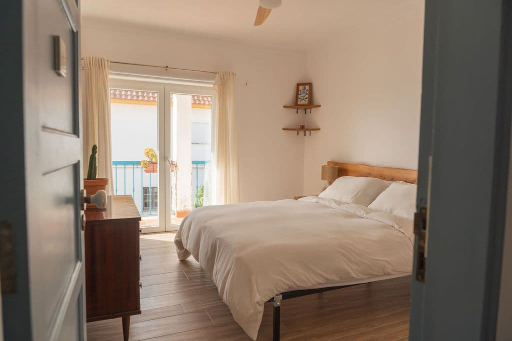 Bright double bedroom with white linens, wooden headboard, and balcony door