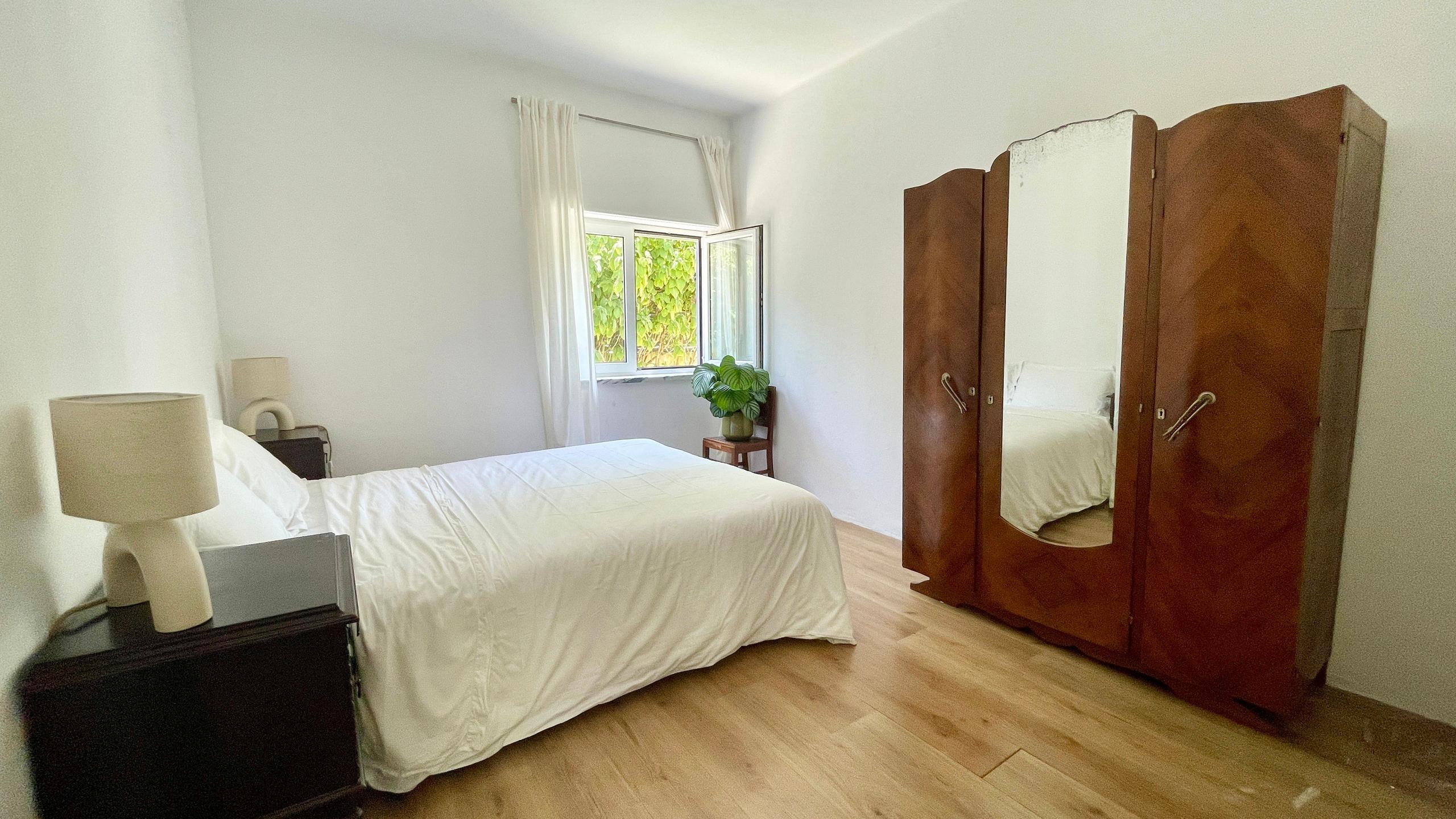 Double bedroom with large wooden wardrobe and white linens