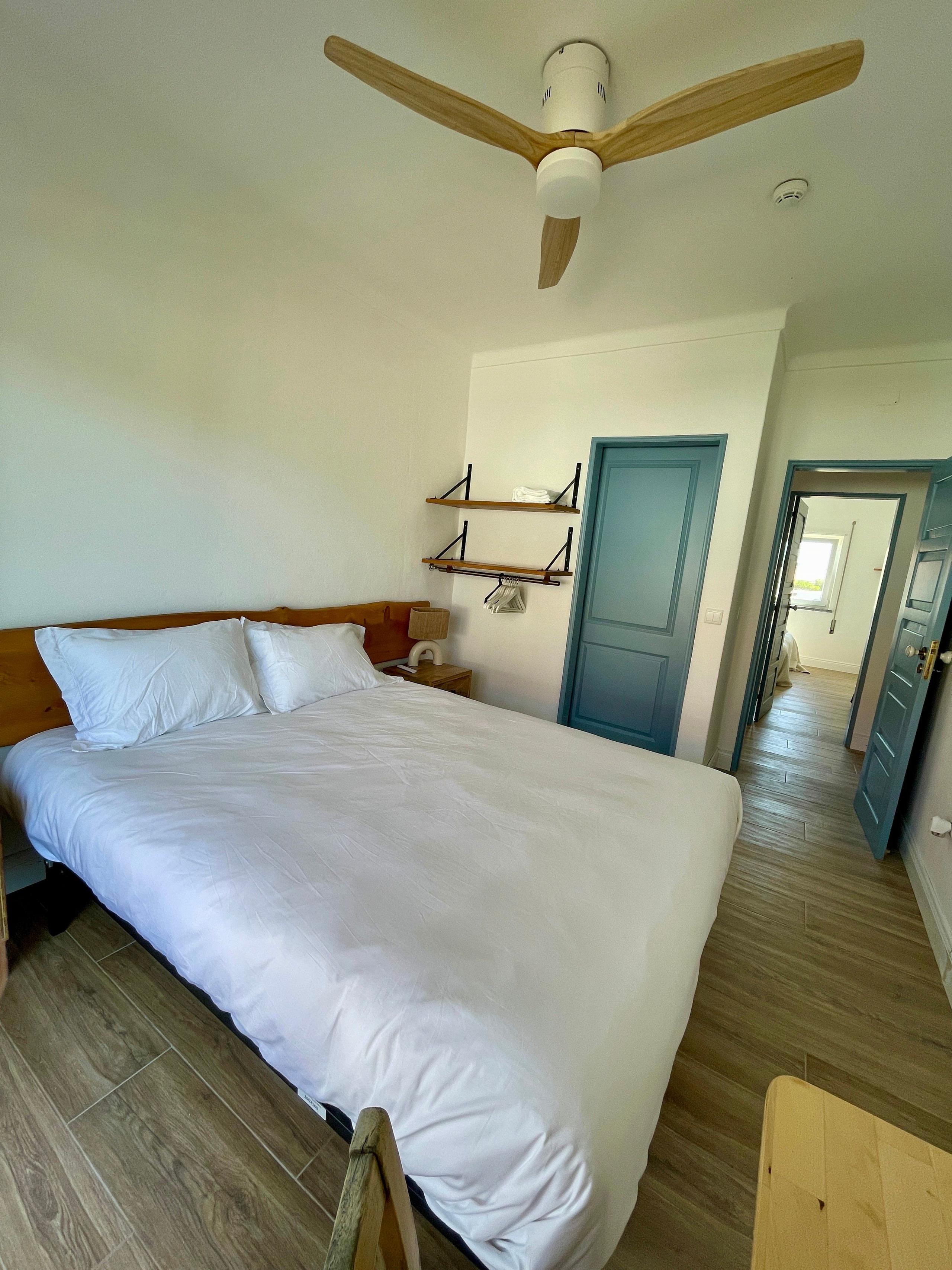Compact double room with ceiling fan, wooden headboard, and blue doors