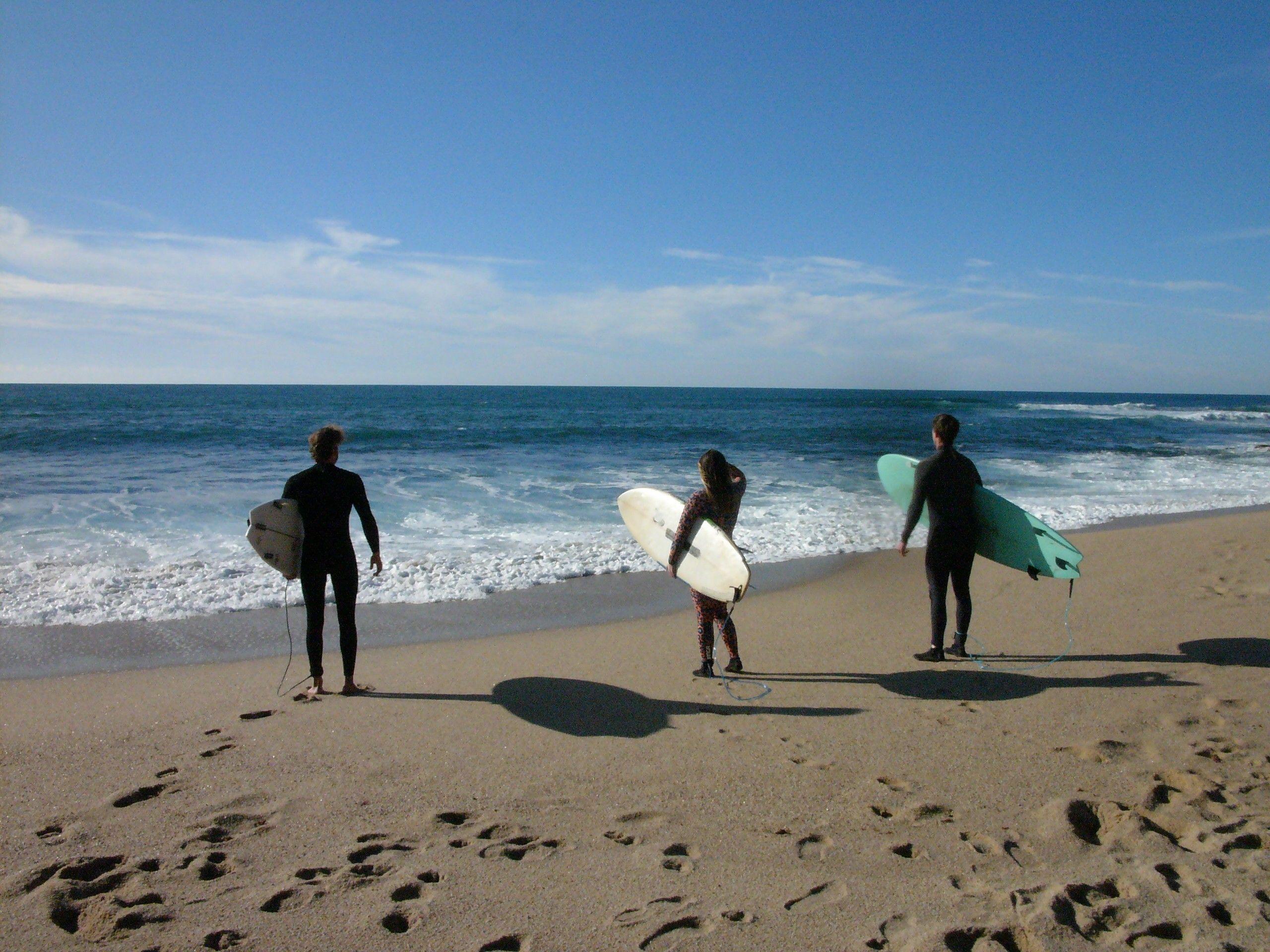 Three residents with surfboards at the beach near Wild Souls Coliving